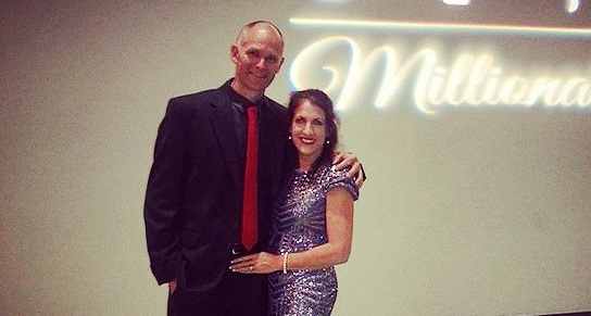 Cathy and Trevor at a network marketing event standing under a millionaire sign