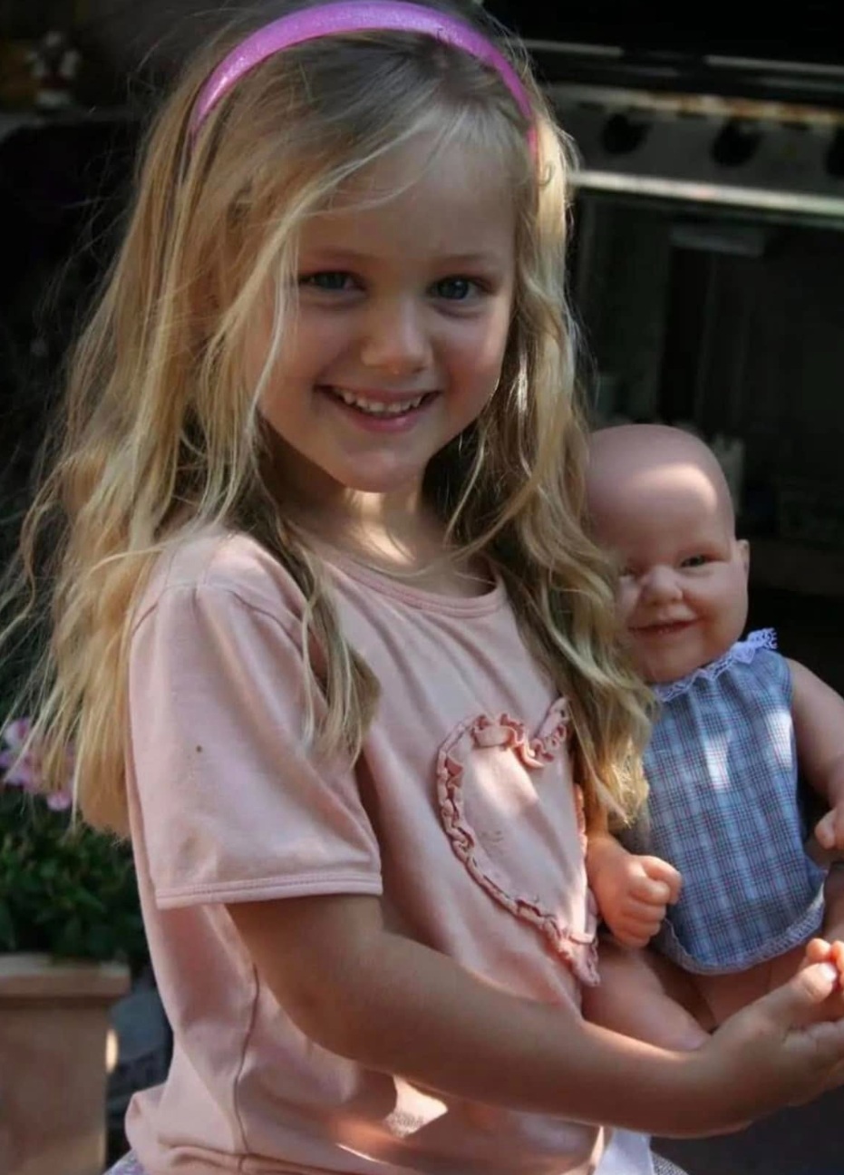 Amber as a young child smiling while holding her doll