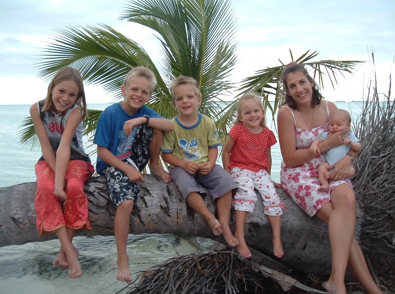 Cathy sitting with young children on a palm log beside the sea on the Cocos Islands